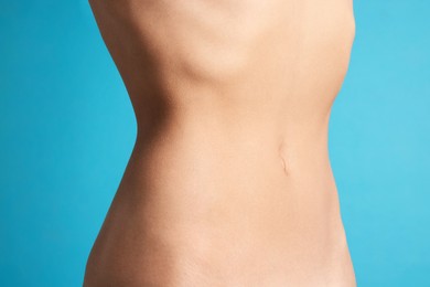 Photo of Woman with flat belly on light blue background, closeup