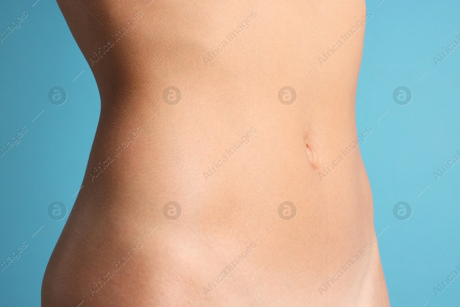Woman with flat belly on light blue background, closeup Photo of Woman with flat belly on light blue background, closeup