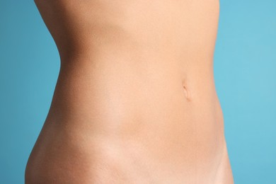 Photo of Woman with flat belly on light blue background, closeup