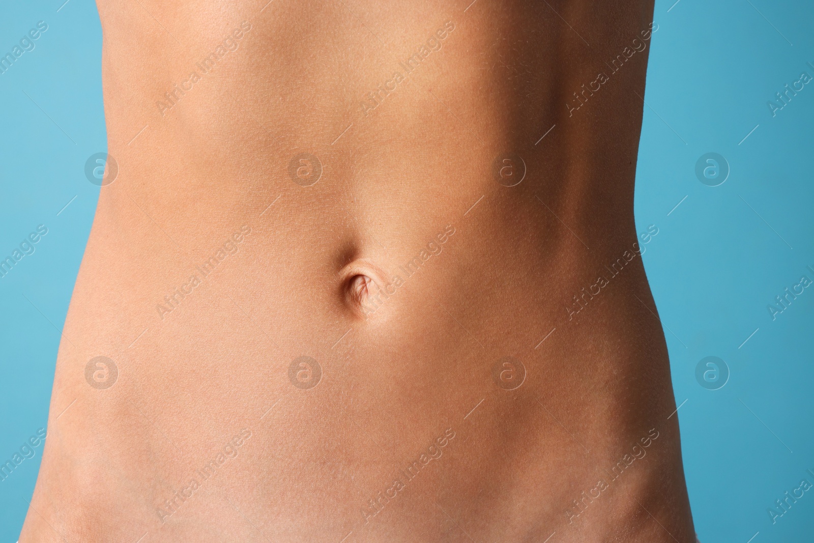 Woman with flat belly on light blue background, closeup Photo of Woman with flat belly on light blue background, closeup
