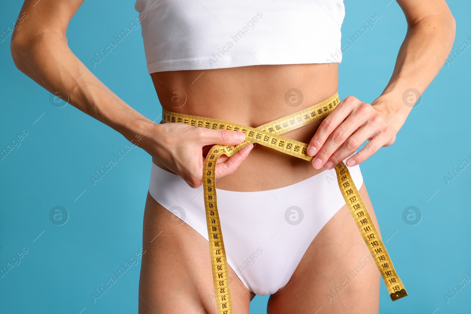 Woman measuring her belly with tape on light blue background, closeup Photo of Woman measuring her belly with tape on light blue background, closeup
