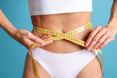 Photo of Woman measuring her belly with tape on light blue background, closeup