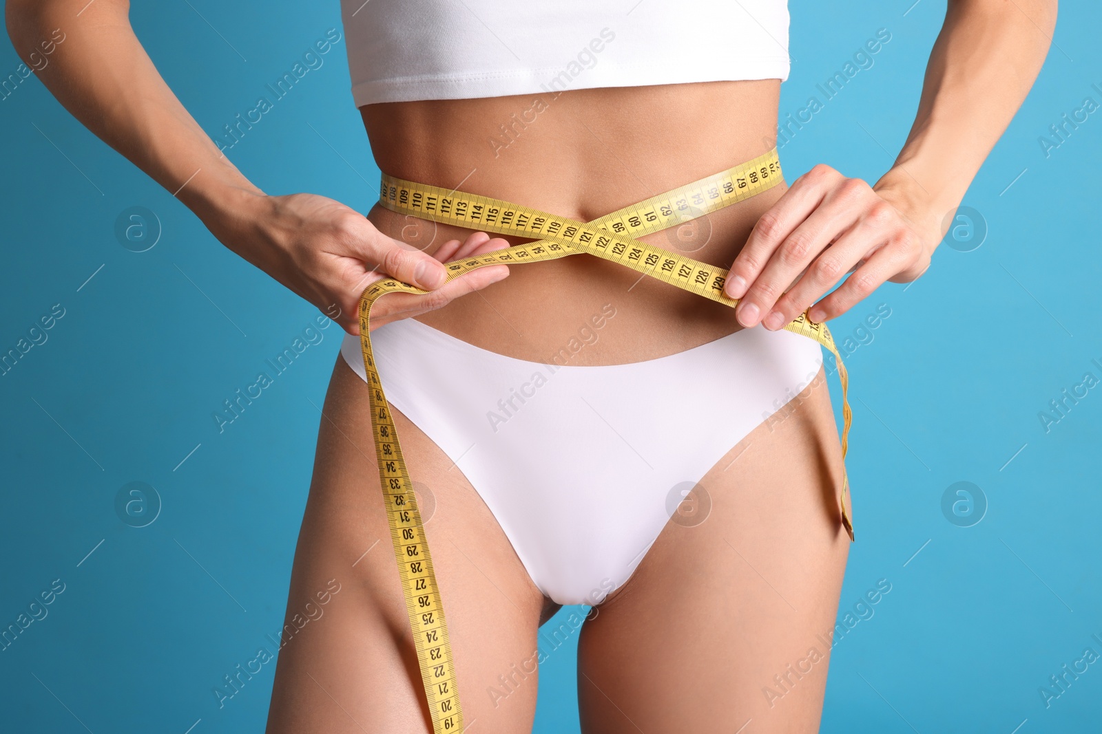 Woman measuring her belly with tape on light blue background, closeup Photo of Woman measuring her belly with tape on light blue background, closeup