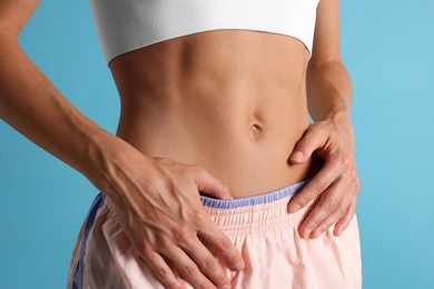 Photo of Woman with flat belly on light blue background, closeup