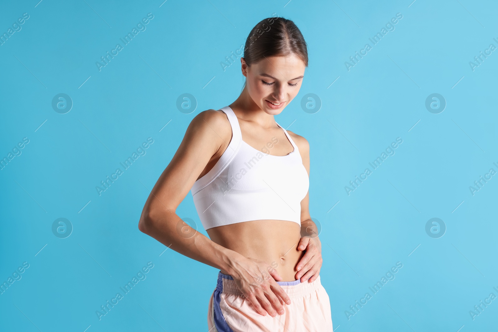 Woman with flat belly on light blue background Photo of Woman with flat belly on light blue background