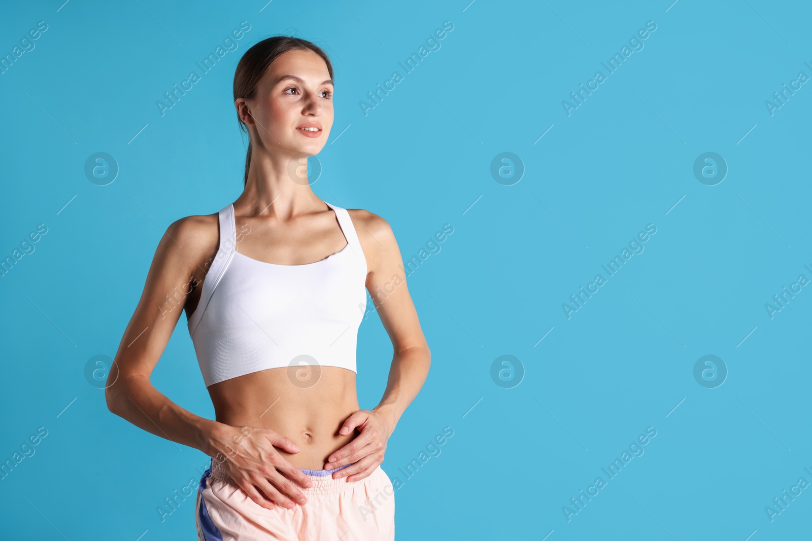 Woman with flat belly on light blue background, space for text Photo of Woman with flat belly on light blue background, space for text