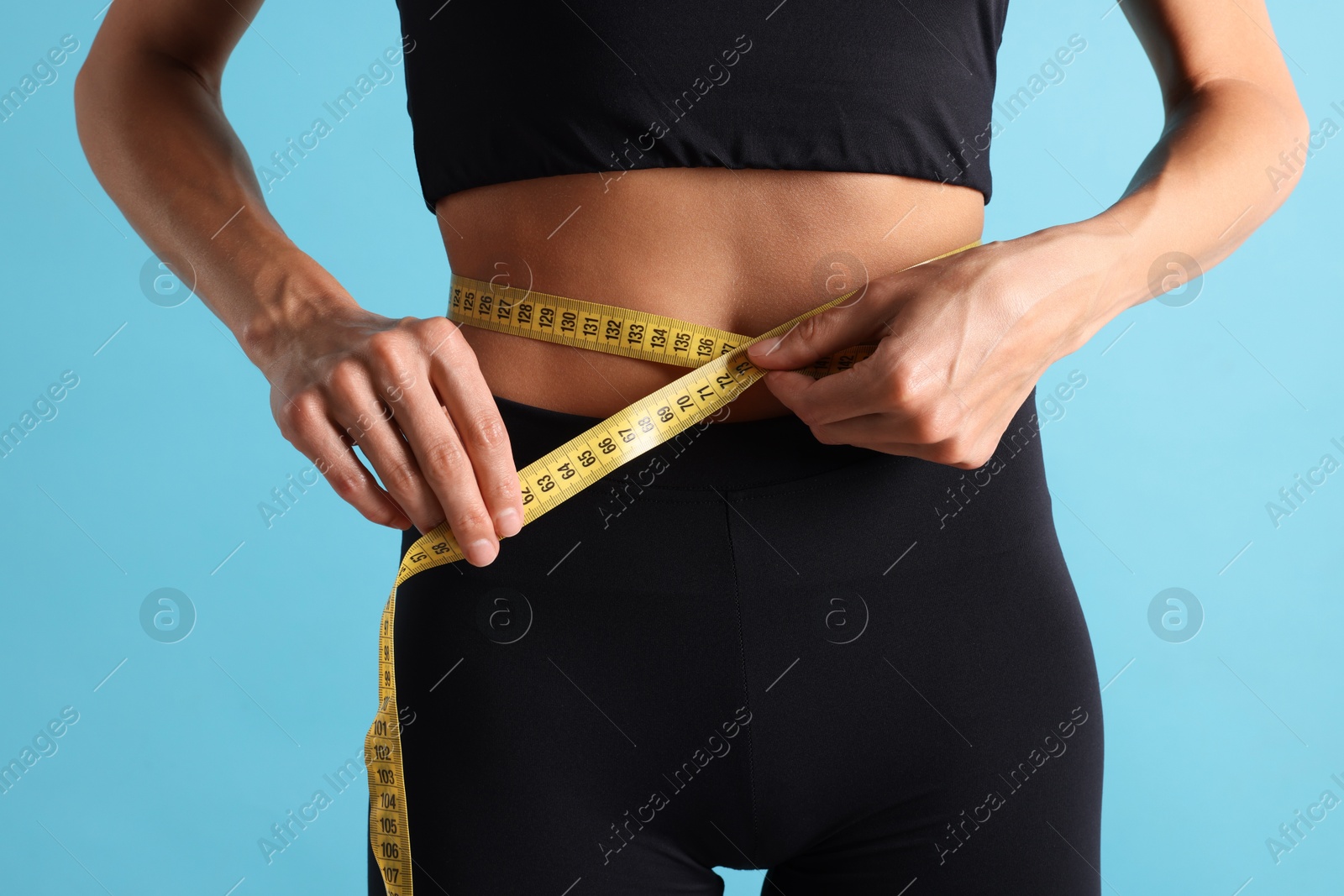 Woman measuring her belly with tape on light blue background, closeup Photo of Woman measuring her belly with tape on light blue background, closeup