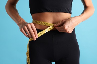 Photo of Woman measuring her belly with tape on light blue background, closeup