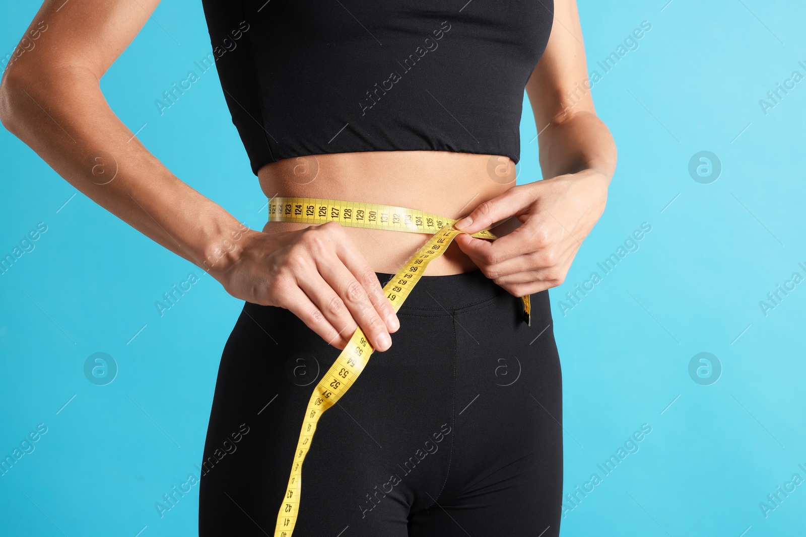 Woman measuring her belly with tape on light blue background, closeup Photo of Woman measuring her belly with tape on light blue background, closeup