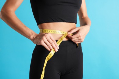Photo of Woman measuring her belly with tape on light blue background, closeup