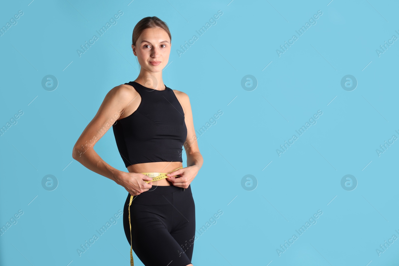 Woman measuring her belly with tape on light blue background, space for text Photo of Woman measuring her belly with tape on light blue background, space for text