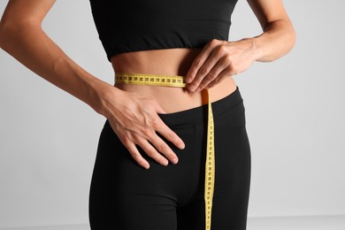 Photo of Woman measuring her belly with tape on light grey background, closeup