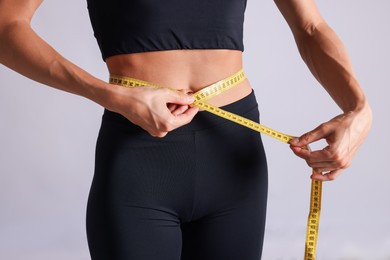 Photo of Woman measuring her belly with tape on light grey background, closeup