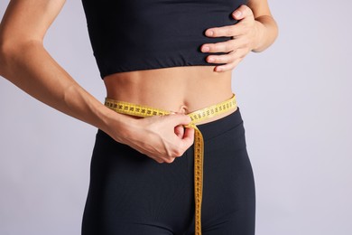 Photo of Woman measuring her belly with tape on light grey background, closeup