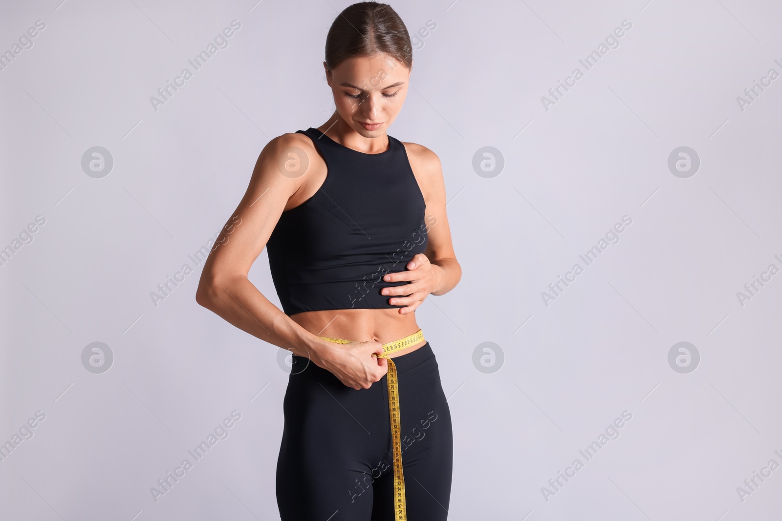 Woman measuring her belly with tape on light grey background Photo of Woman measuring her belly with tape on light grey background