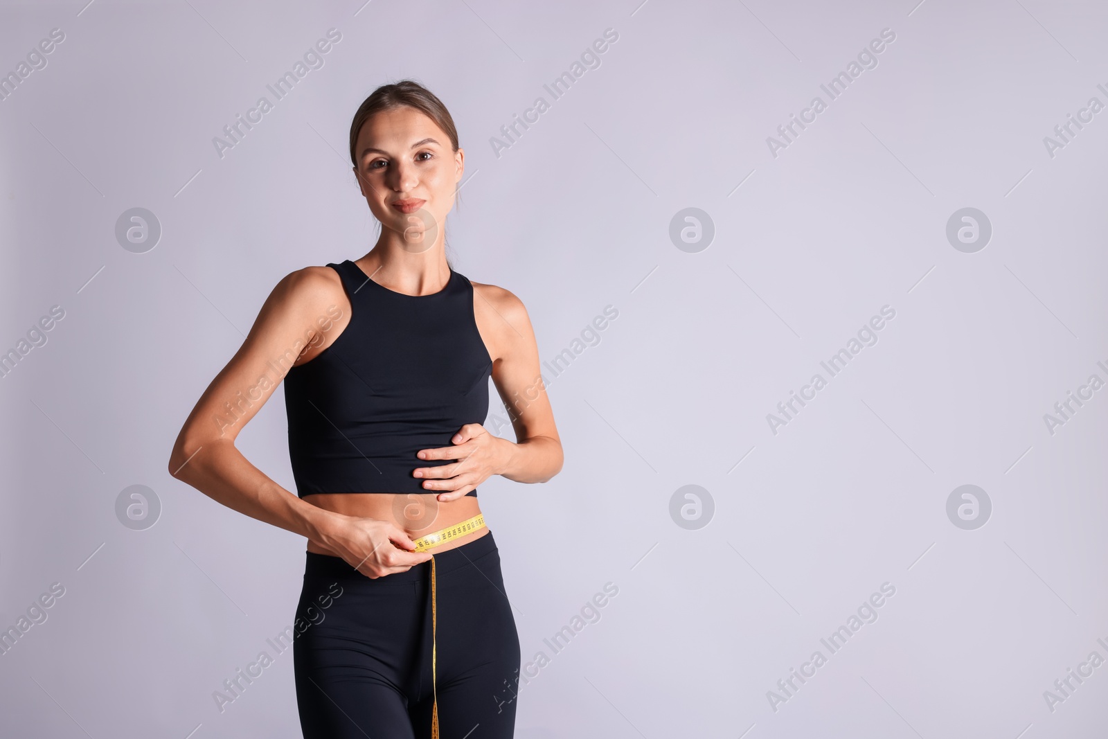 Woman measuring her belly with tape on light grey background, space for text Photo of Woman measuring her belly with tape on light grey background, space for text