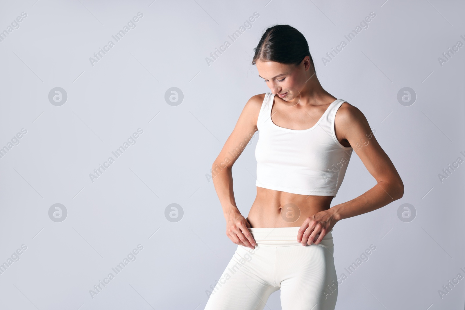Woman with flat belly on light grey background, space for text Photo of Woman with flat belly on light grey background, space for text