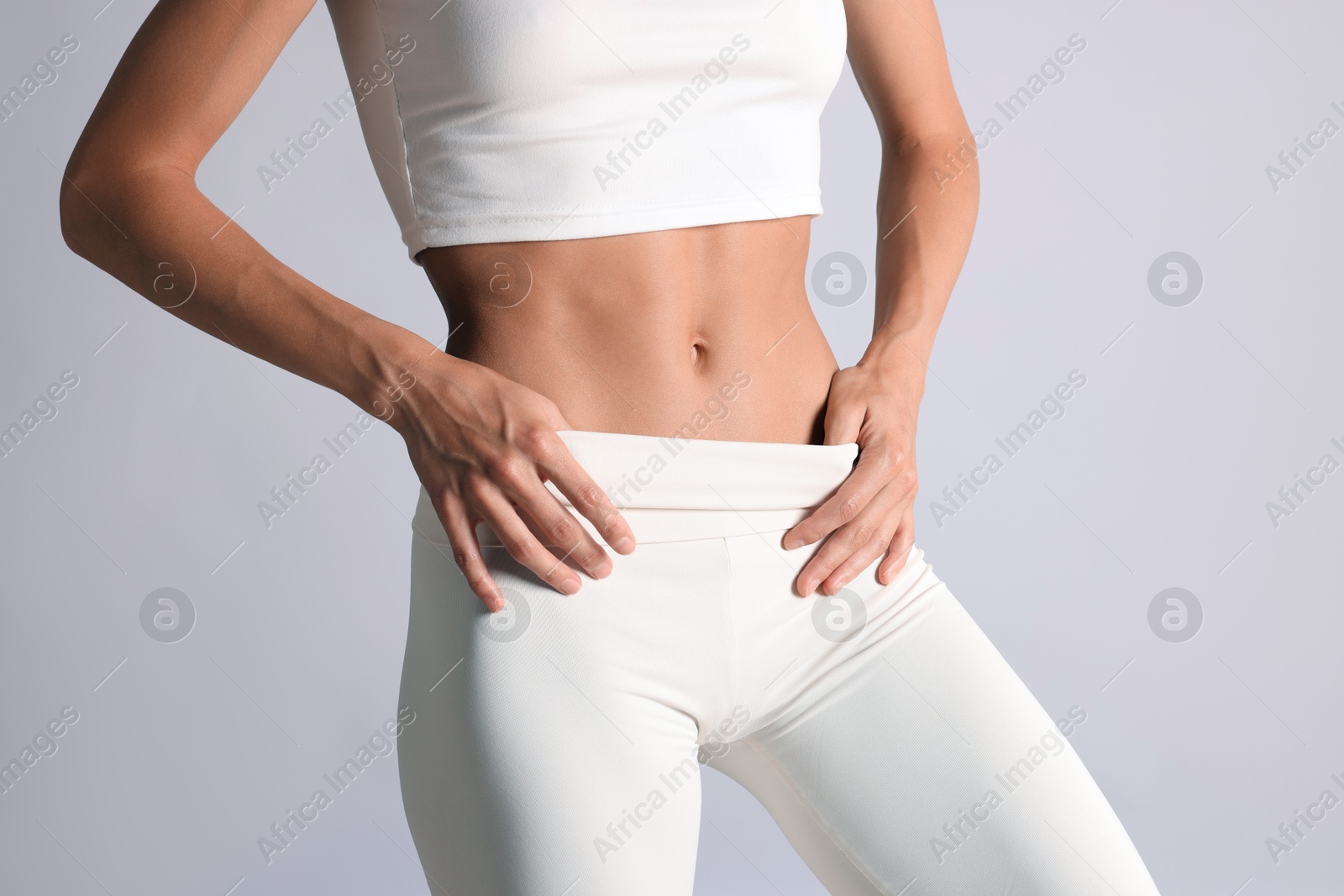 Woman with flat belly on light grey background, closeup Photo of Woman with flat belly on light grey background, closeup