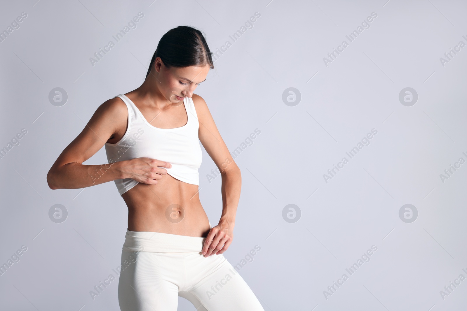 Woman with flat belly on light grey background, space for text Photo of Woman with flat belly on light grey background, space for text