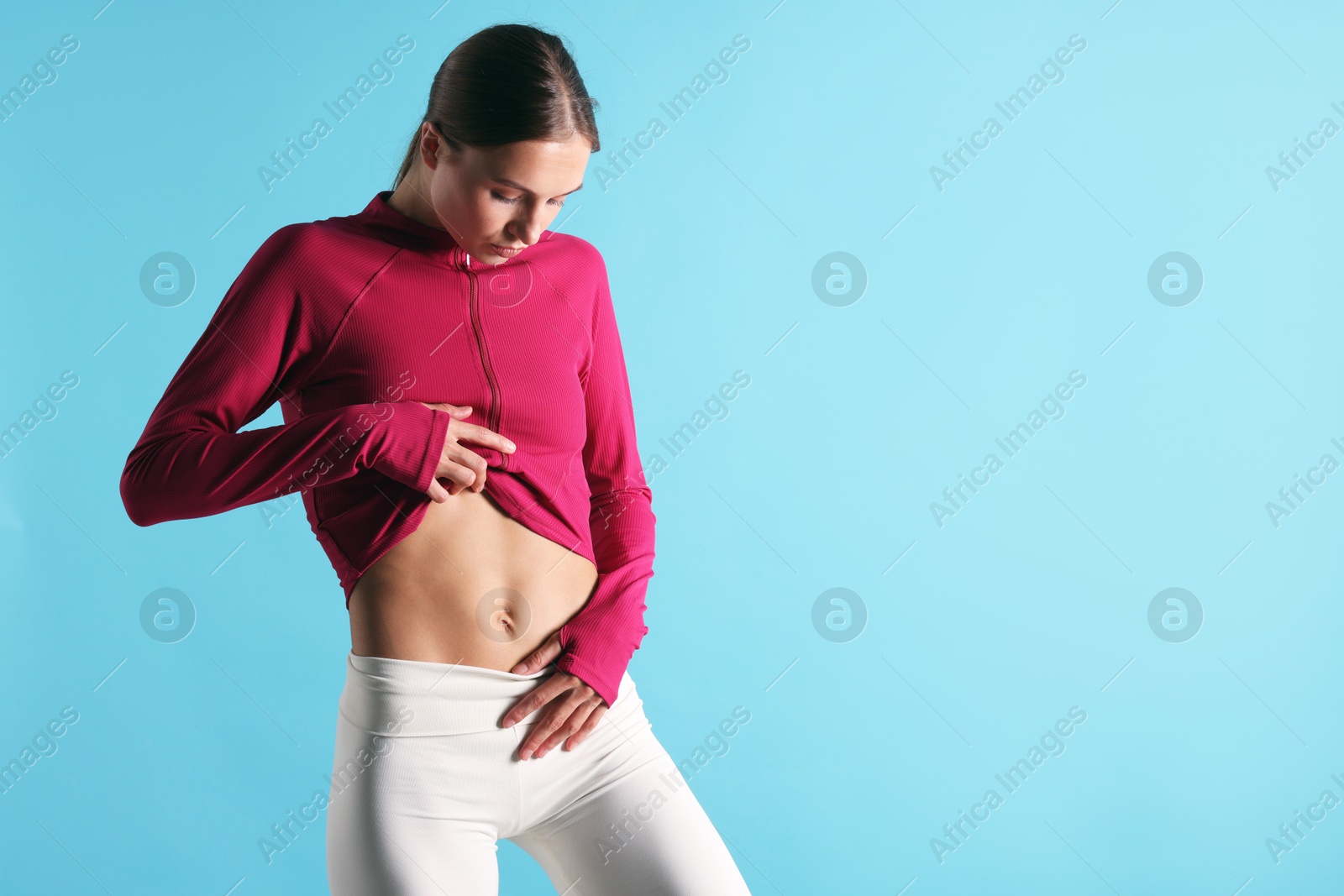 Woman with flat belly on light blue background, space for text Photo of Woman with flat belly on light blue background, space for text