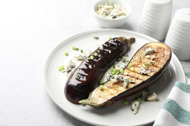 Photo of Slices of grilled eggplant with green onion and blue cheese on white table, closeup. Space for text