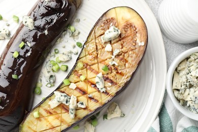 Photo of Slices of grilled eggplant with green onion and blue cheese on white table, flat lay