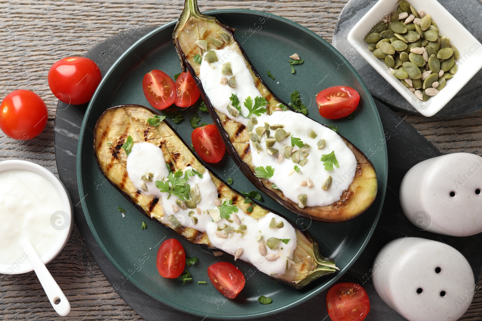 Slices of grilled eggplant with pumpkin seeds, tomatoes and yoghurt on wooden table, flat lay Photo of Slices of grilled eggplant with pumpkin seeds, tomatoes and yoghurt on wooden table, flat lay