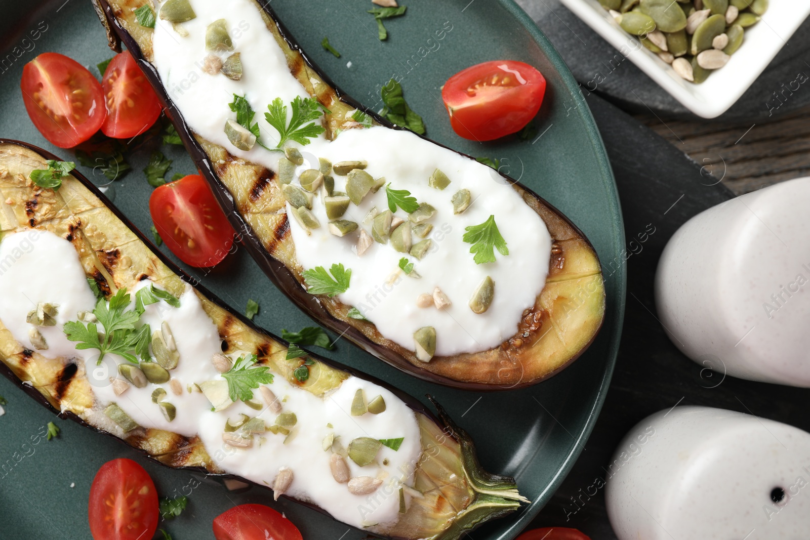Slices of grilled eggplant with pumpkin seeds, tomatoes and yoghurt on wooden table, flat lay Photo of Slices of grilled eggplant with pumpkin seeds, tomatoes and yoghurt on wooden table, flat lay