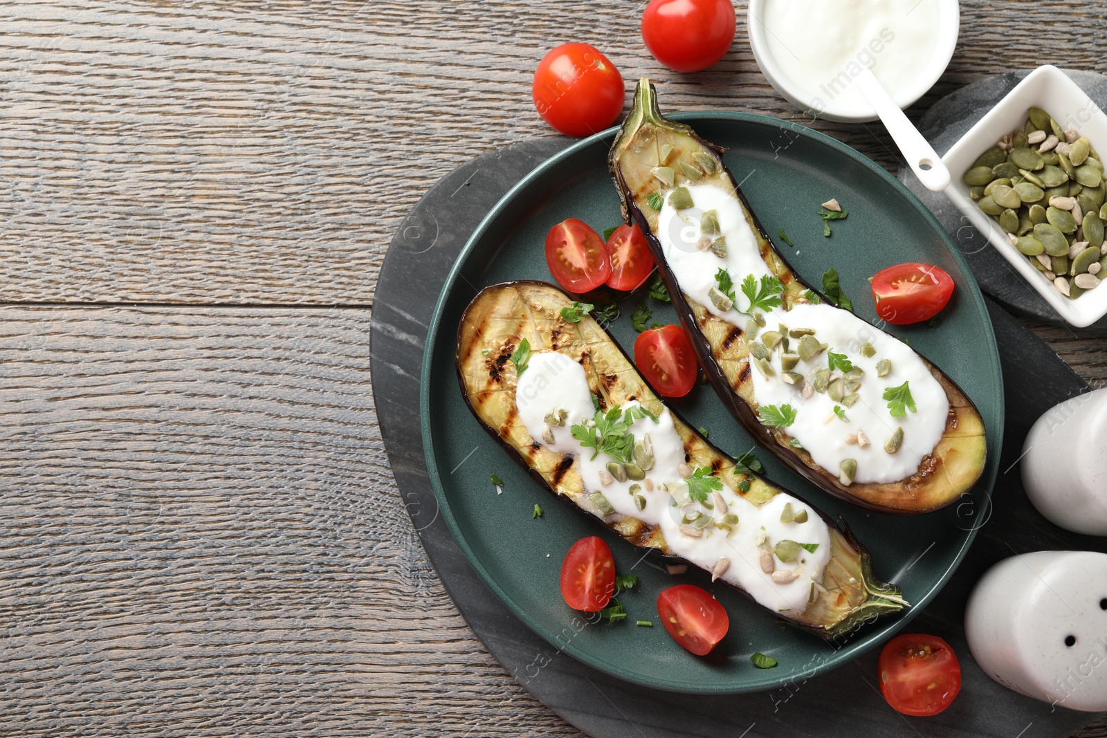 Slices of grilled eggplant with pumpkin seeds, tomatoes and yoghurt on wooden table, flat lay. Space for text Photo of Slices of grilled eggplant with pumpkin seeds, tomatoes and yoghurt on wooden table, flat lay. Space for text