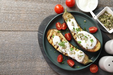 Photo of Slices of grilled eggplant with pumpkin seeds, tomatoes and yoghurt on wooden table, flat lay. Space for text