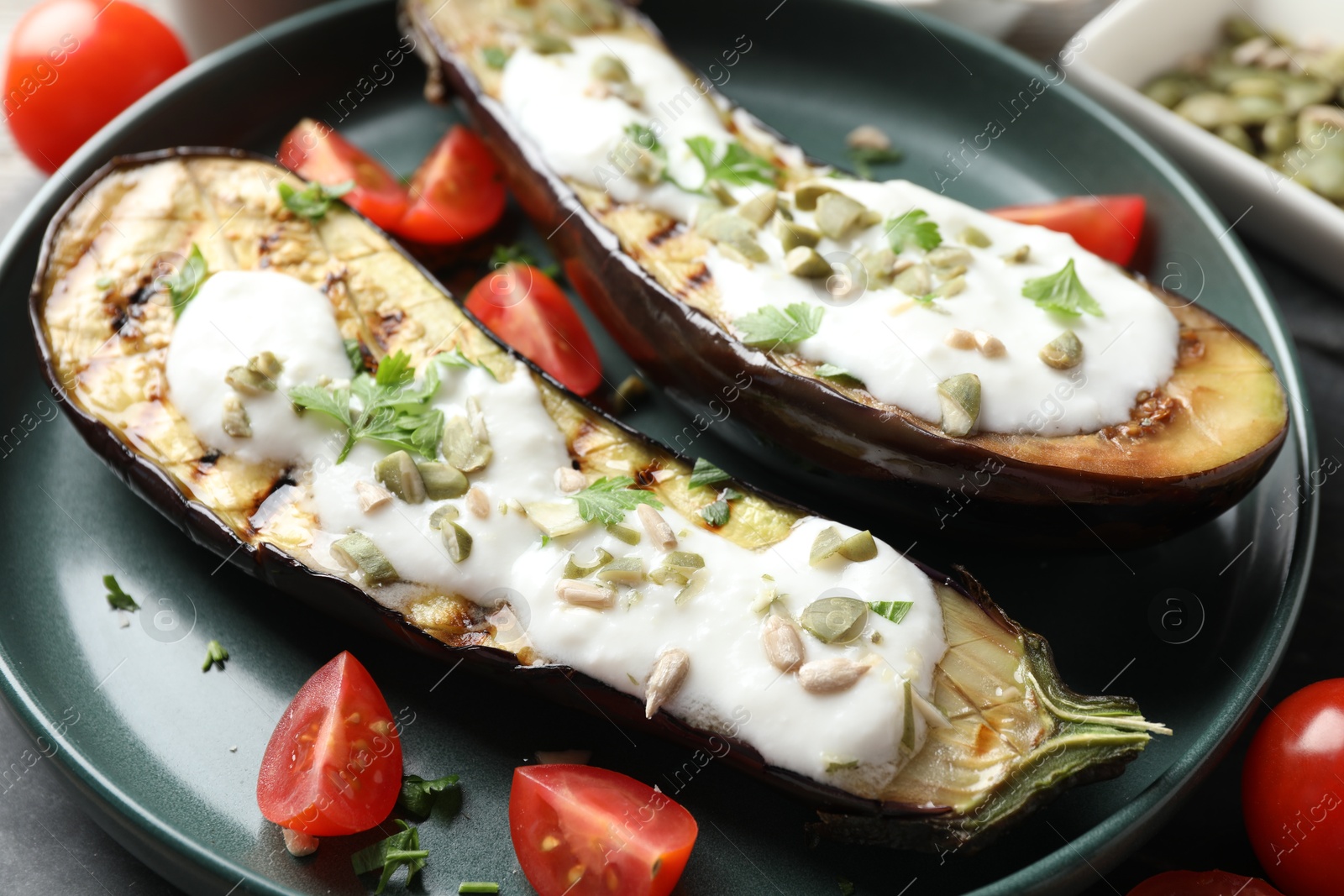Photo of Slices of grilled eggplant with pumpkin seeds, tomatoes and yoghurt on table, closeup