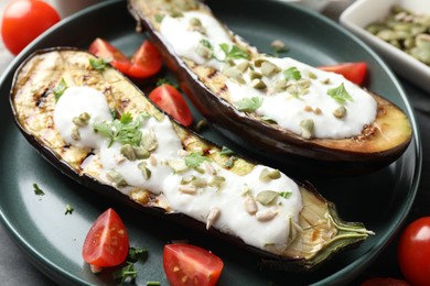 Photo of Slices of grilled eggplant with pumpkin seeds, tomatoes and yoghurt on table, closeup