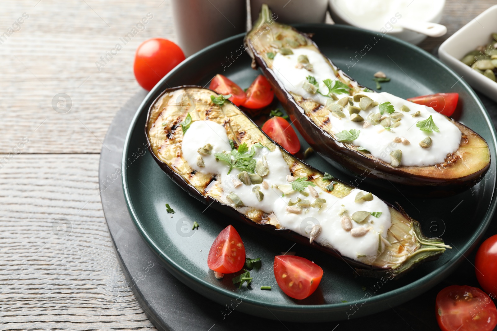 Slices of grilled eggplant with pumpkin seeds, tomatoes and yoghurt on wooden table, closeup Photo of Slices of grilled eggplant with pumpkin seeds, tomatoes and yoghurt on wooden table, closeup