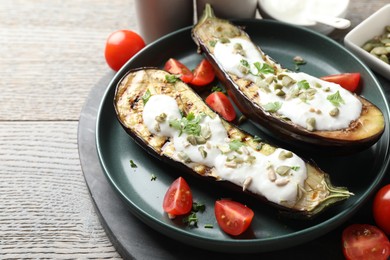 Photo of Slices of grilled eggplant with pumpkin seeds, tomatoes and yoghurt on wooden table, closeup