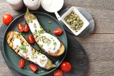 Photo of Slices of grilled eggplant with pumpkin seeds, tomatoes and yoghurt on wooden table, flat lay