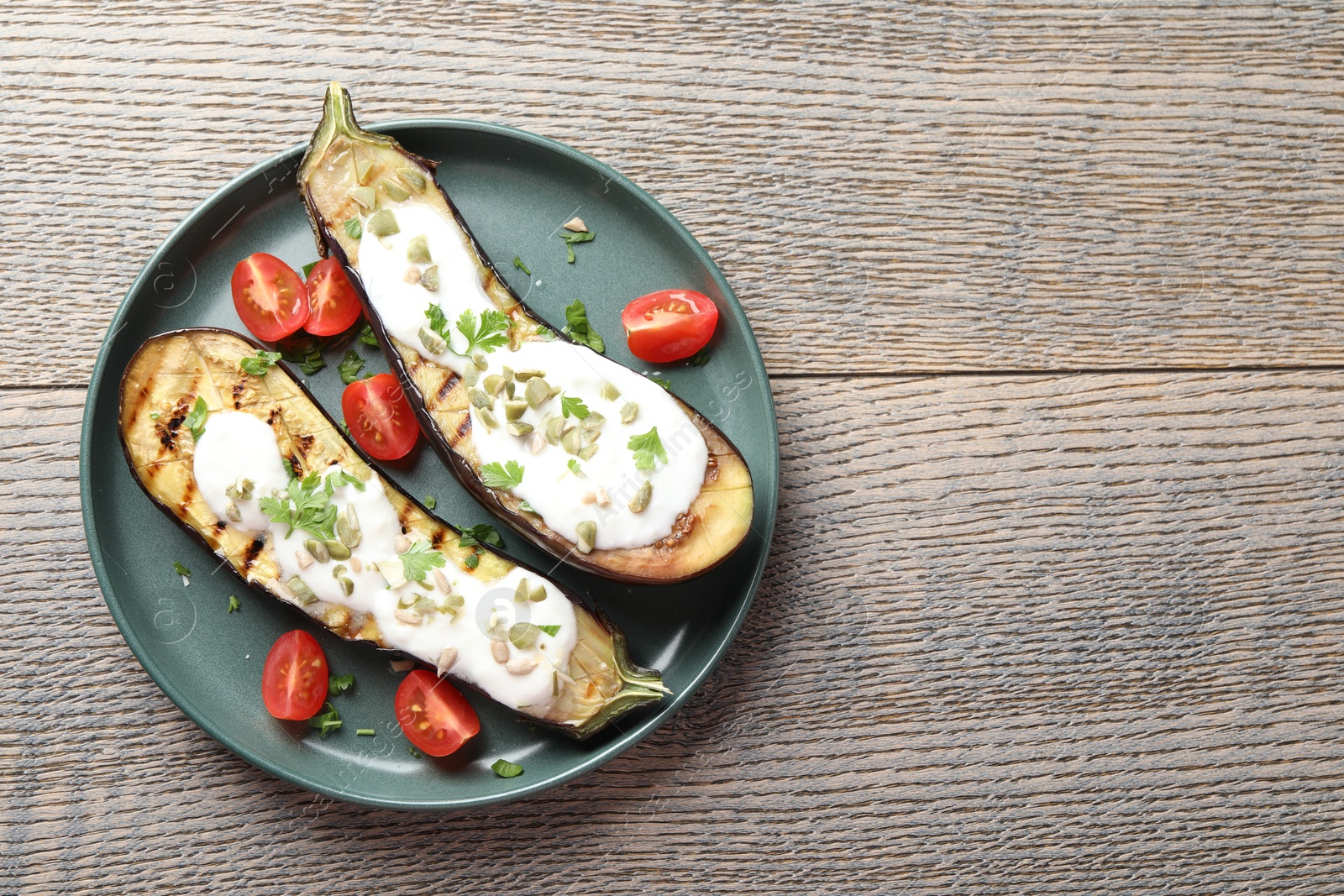 Photo of Slices of grilled eggplant with pumpkin seeds, tomatoes and yoghurt on wooden table, top view. Space for text