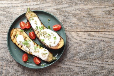 Photo of Slices of grilled eggplant with pumpkin seeds, tomatoes and yoghurt on wooden table, top view. Space for text