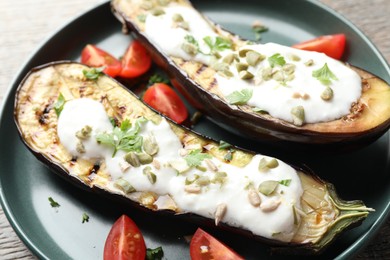 Photo of Slices of grilled eggplant with pumpkin seeds, tomatoes and yoghurt on wooden table, closeup