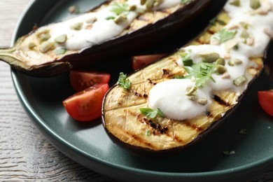 Photo of Slices of grilled eggplant with pumpkin seeds, tomatoes and yoghurt on wooden table, closeup