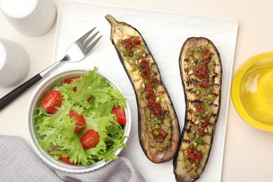 Photo of Slices of grilled eggplant with sun dried tomatoes, pesto and salad on white table, flat lay