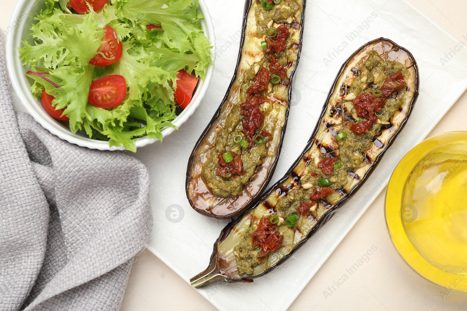 Photo of Slices of grilled eggplant with sun dried tomatoes, pesto and salad on white table, flat lay