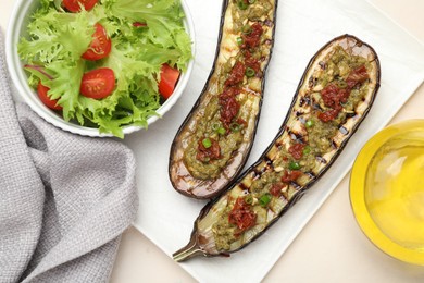 Photo of Slices of grilled eggplant with sun dried tomatoes, pesto and salad on white table, flat lay