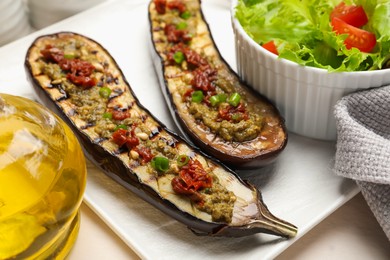Photo of Slices of grilled eggplant with sun dried tomatoes, pesto and salad on white table, closeup