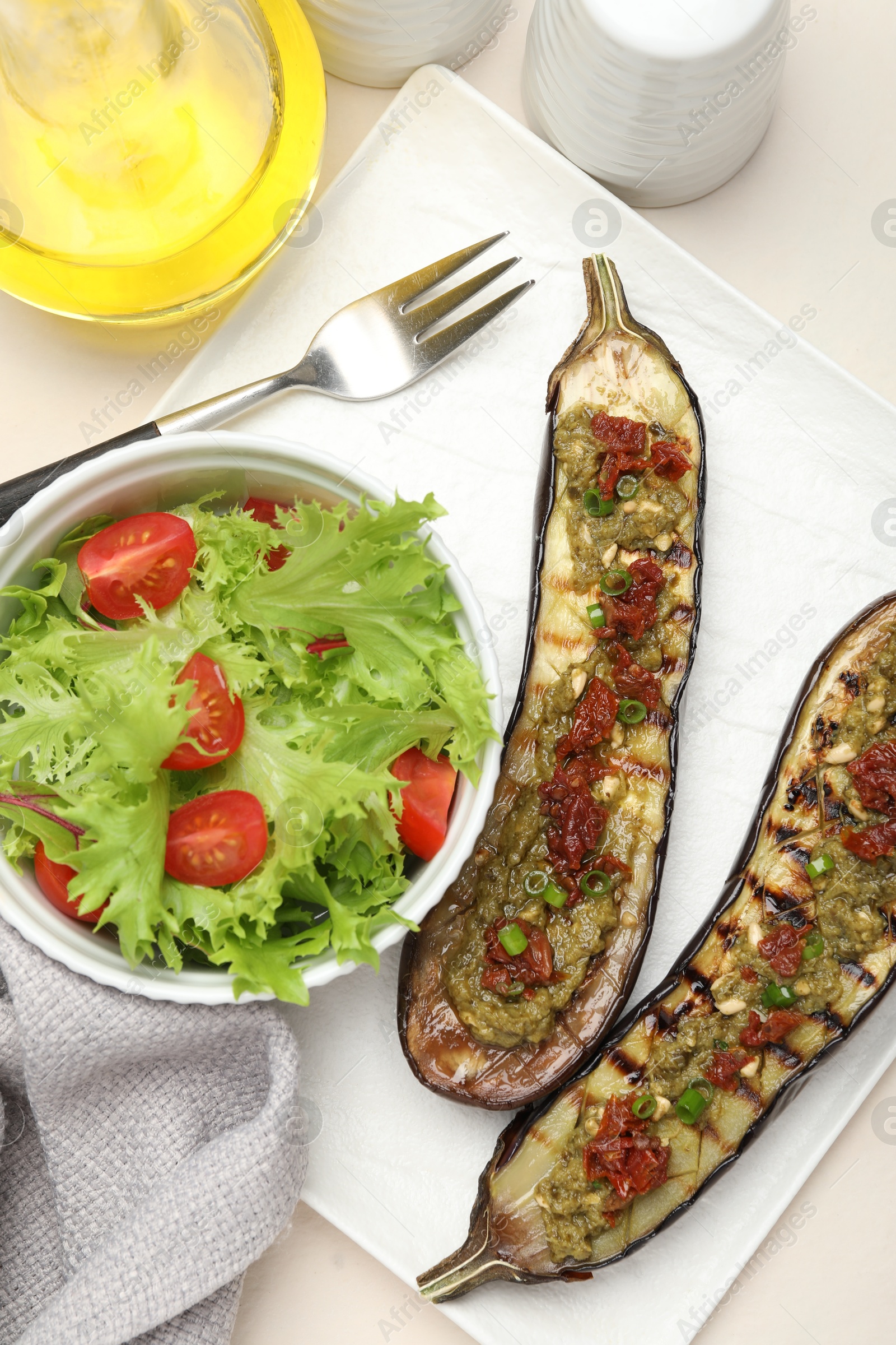 Photo of Slices of grilled eggplant with sun dried tomatoes, pesto and salad on white table, flat lay