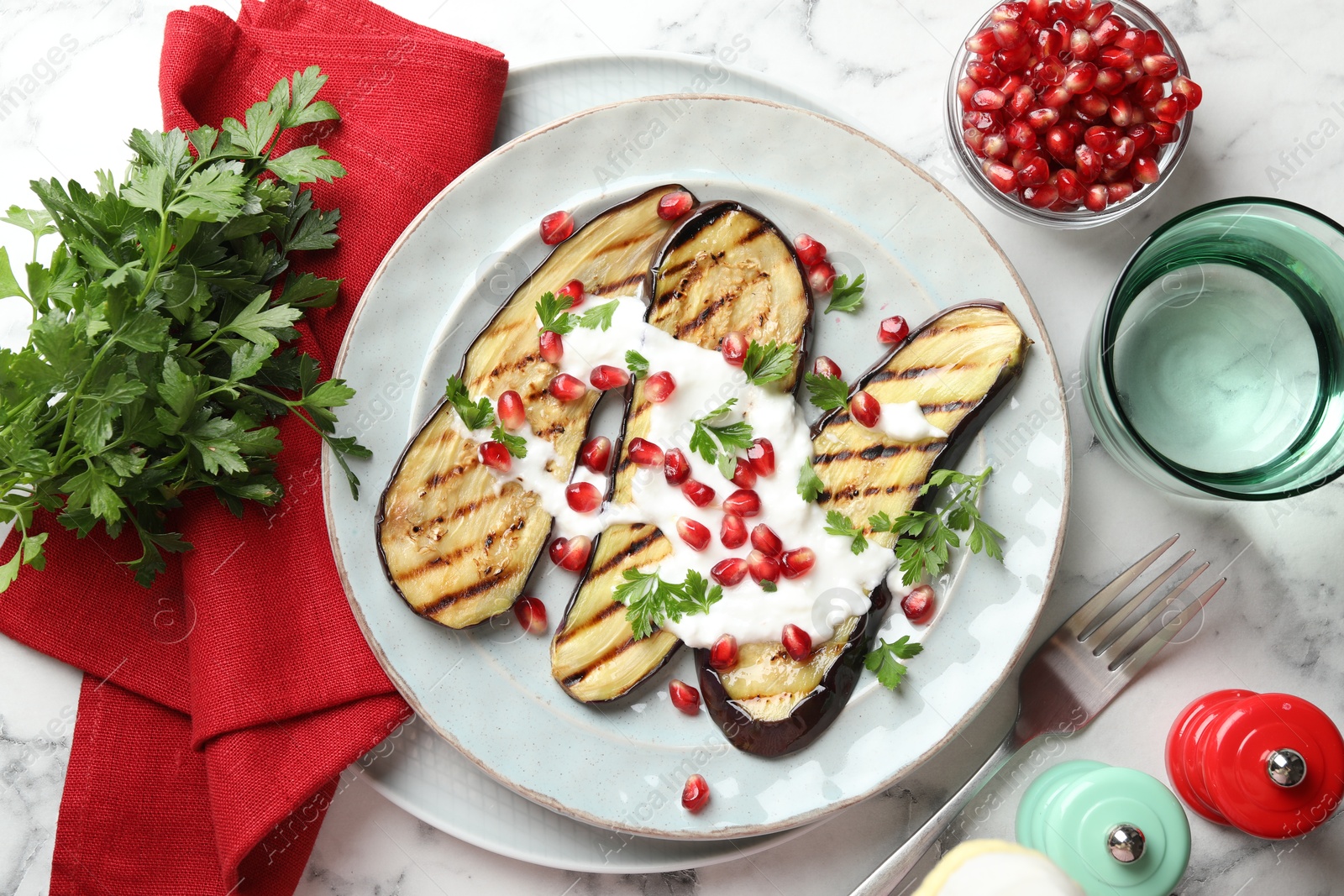 Slices of grilled eggplant with pomegranate seeds and yoghurt on white marble table, flat lay Photo of Slices of grilled eggplant with pomegranate seeds and yoghurt on white marble table, flat lay