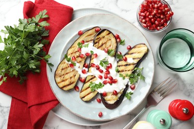 Photo of Slices of grilled eggplant with pomegranate seeds and yoghurt on white marble table, flat lay