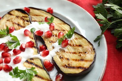Photo of Slices of grilled eggplant with pomegranate seeds and yoghurt on table, closeup