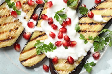 Photo of Slices of grilled eggplant with pomegranate seeds and yoghurt on table