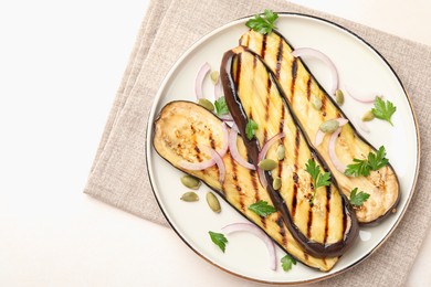 Photo of Slices of grilled eggplant, parsley, pumpkin seeds and onion on white table, top view. Space for text