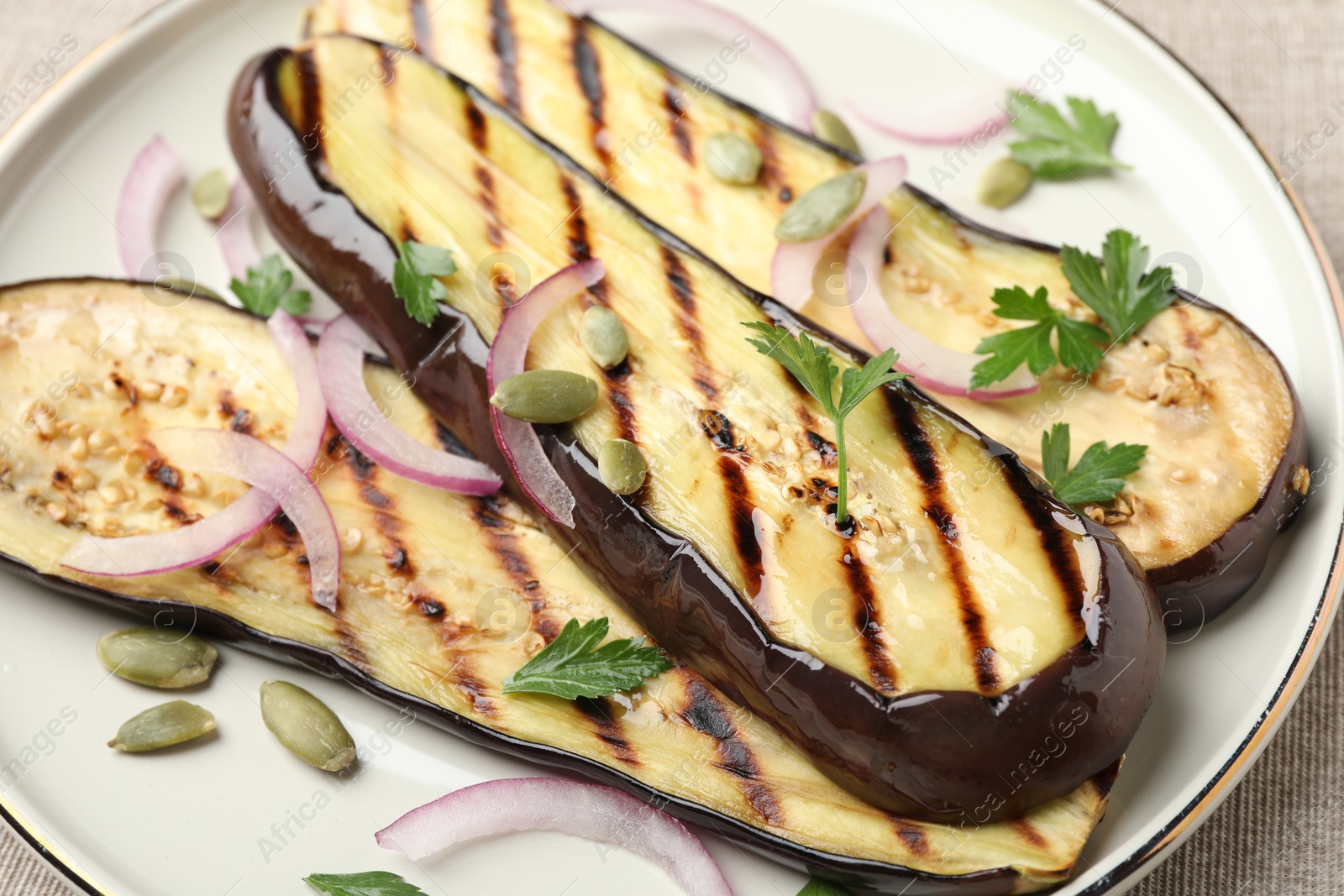 Photo of Slices of grilled eggplant, parsley, pumpkin seeds and onion on table, closeup